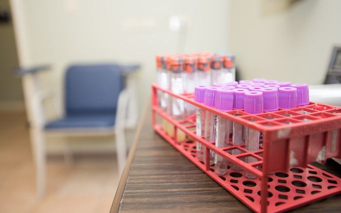 Tubos vacíos para muestras de sangre en una gradilla roja, en el laboratorio de un centro de salud comunitario de Texas. Atrás, la silla de extracción.
