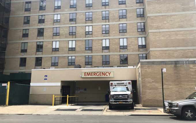 Una ambulancia estacionada en la entrada de emergencias de un hospital de ladrillo en el Bronx, bajo un letrero que dice Emergency.