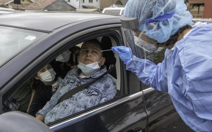 Un hombre de chaqueta de mezclilla espera sentado en su auto mientras una trabajadora con bata y careta le acerca un hisopo a la nariz.